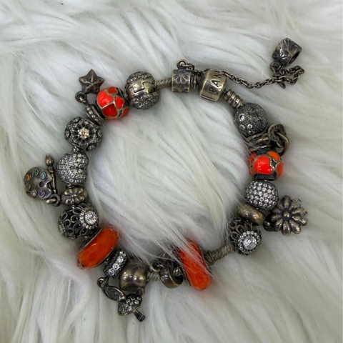 這是一條Pandora 品牌的串珠手鍊，上面配有各種銀製和鮮豔的橘色墜飾。