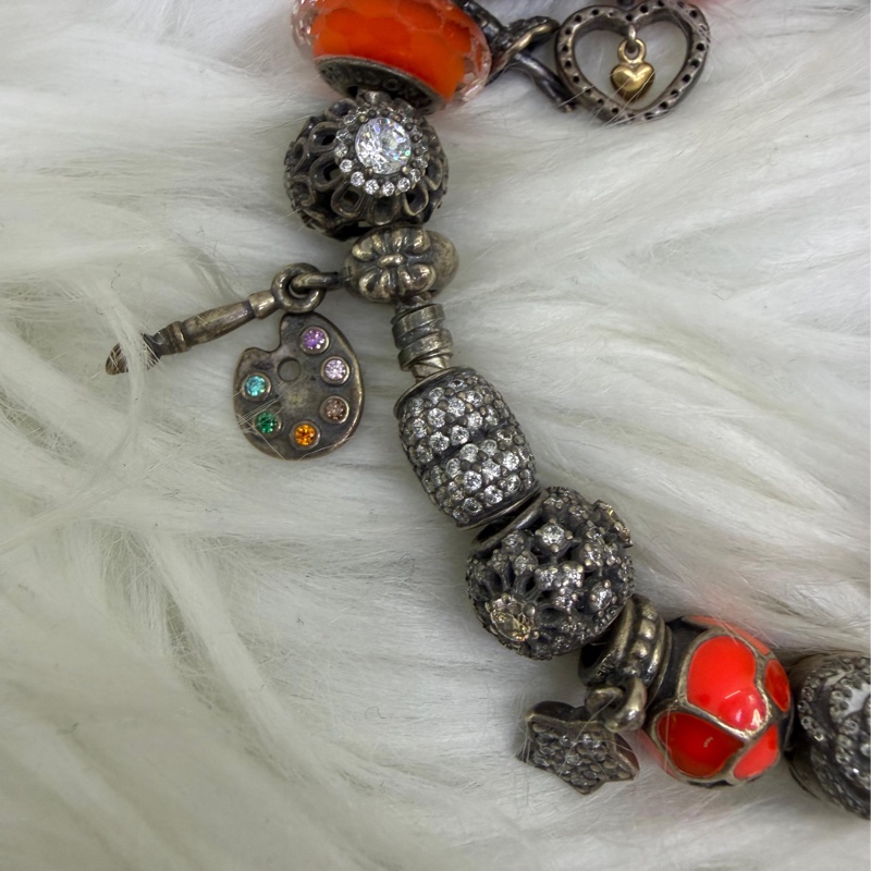 這是一條Pandora 品牌的串珠手鍊，上面配有各種銀製和鮮豔的橘色墜飾。-2