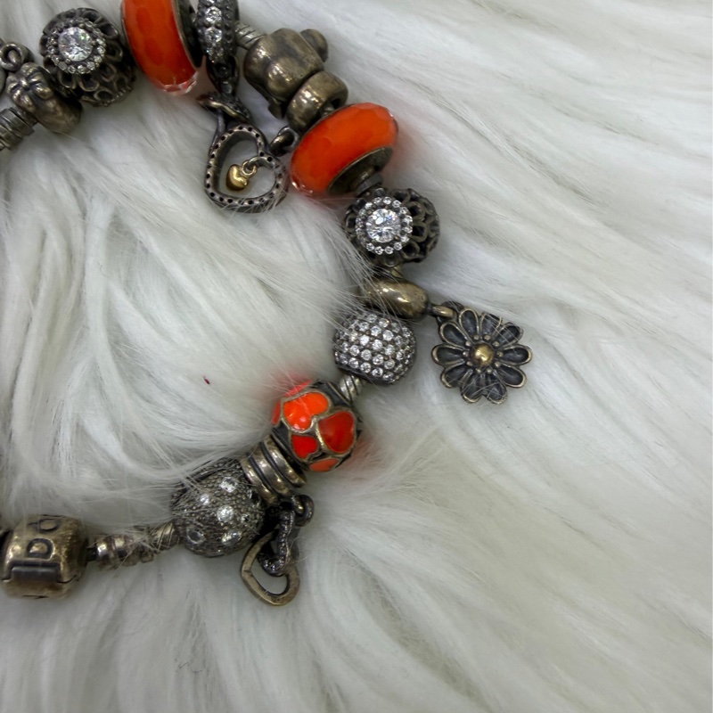 這是一條Pandora 品牌的串珠手鍊，上面配有各種銀製和鮮豔的橘色墜飾。-3
