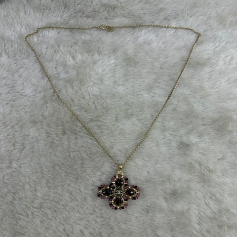 這條 Chanel 品牌項鍊以金屬色細鍊搭配由紫色寶石與經典雙 C Logo 組成的花卉狀墜飾。