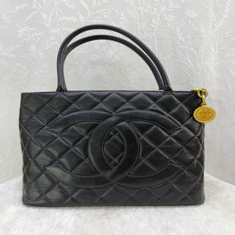 這款經典的黑色 CHANEL 復刻托特包 (Medallion Tote) 採用魚子醬牛皮製成，配有顯眼的金色 CC 吊飾