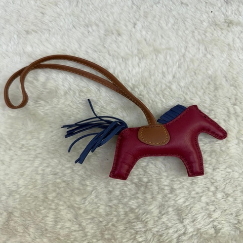 這是一款 Hermès Rodeo 小馬掛飾，其特色為酒紅色小羊皮主體搭配藍色鬃毛與馬尾