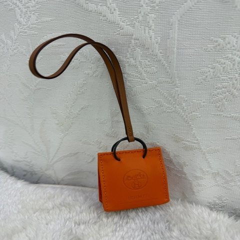 這是一款 Hermes Milo 皮革 Sac Orange 掛飾，特色在於其縮小版的橘色紙袋造型。
