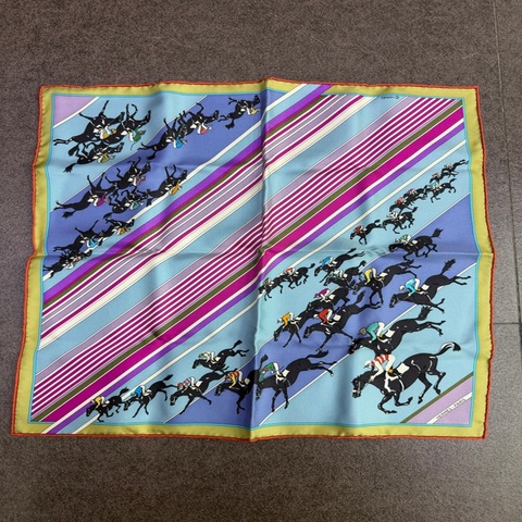 這是愛馬仕 (Hermès) 的 "Les Courses" (賽馬) 系列絲巾，圖案描繪了彩色的賽馬場景與斜條紋設計。